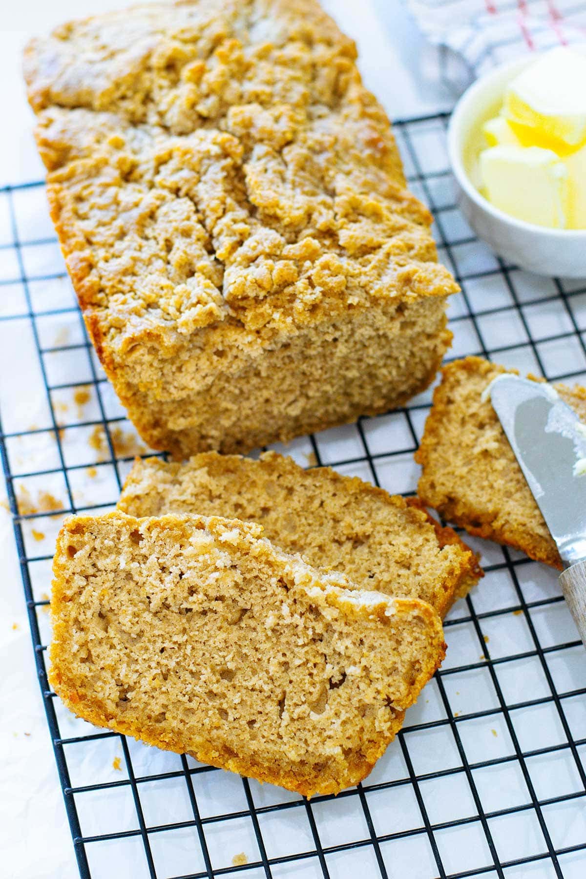 Slices of buttery beer bread on a baking rack with the loaf and butter in the background.