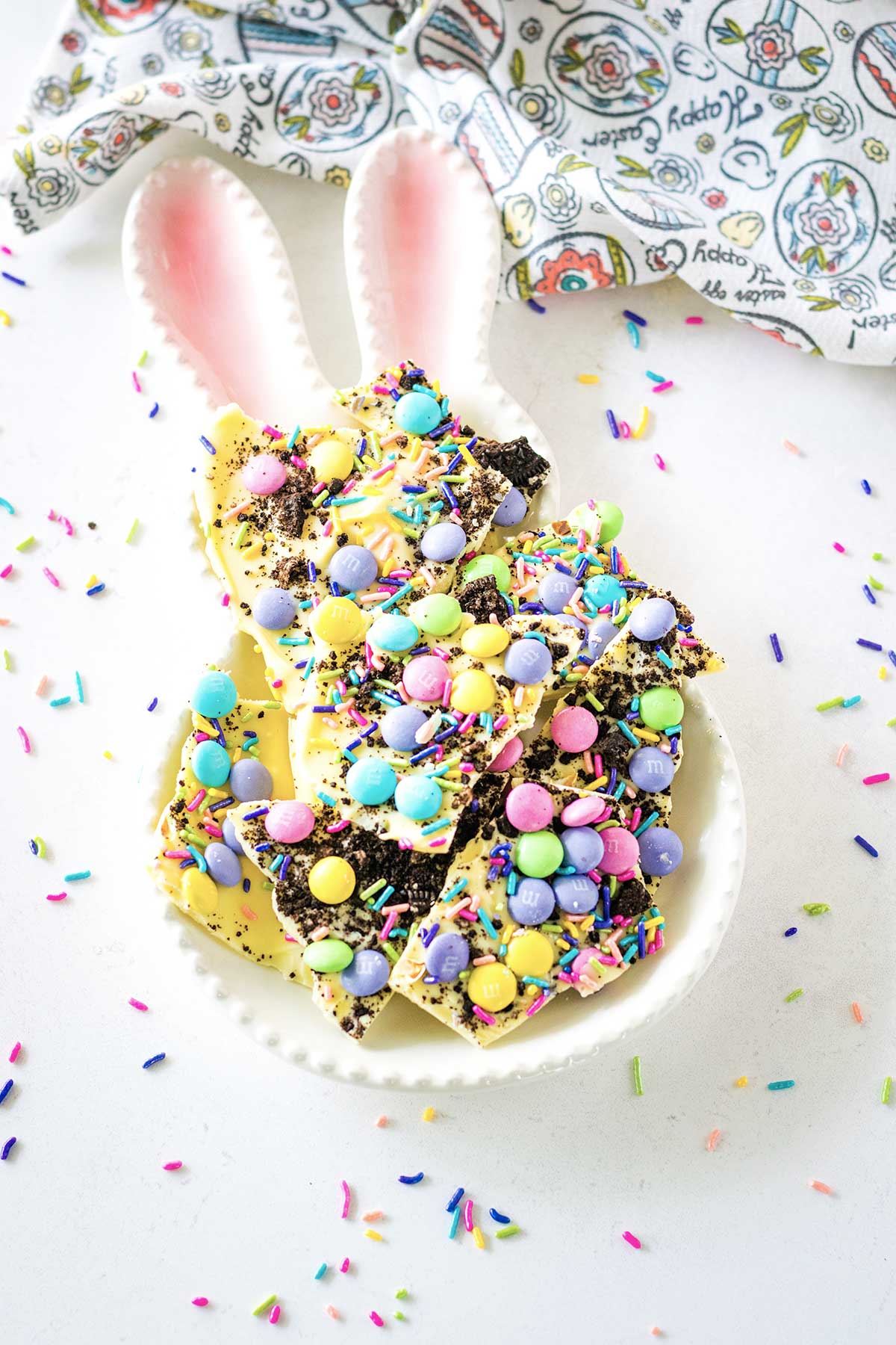 Oreo Bark in a bunny-shaped serving dish with sprinkles scattered about on a white tray. 
