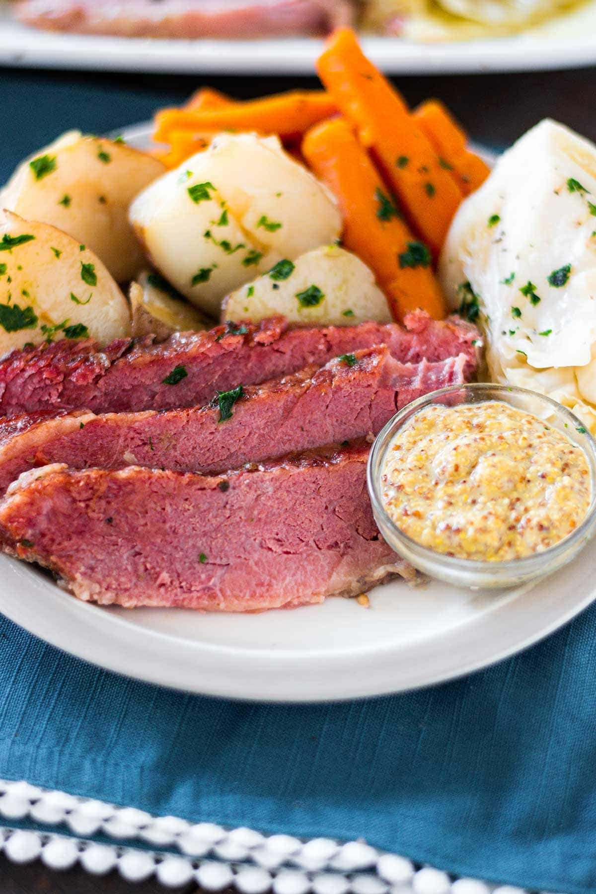 Corn beef and cabbage meal with potatoes and carrots on a white plate set on a blue placemat.