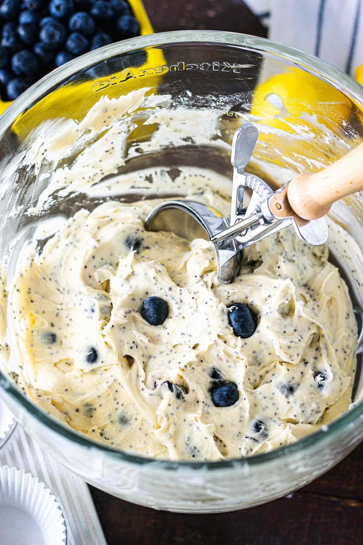Blueberry lemon poppy seed muffin batter with an ice cream scoop in the batter bowl.