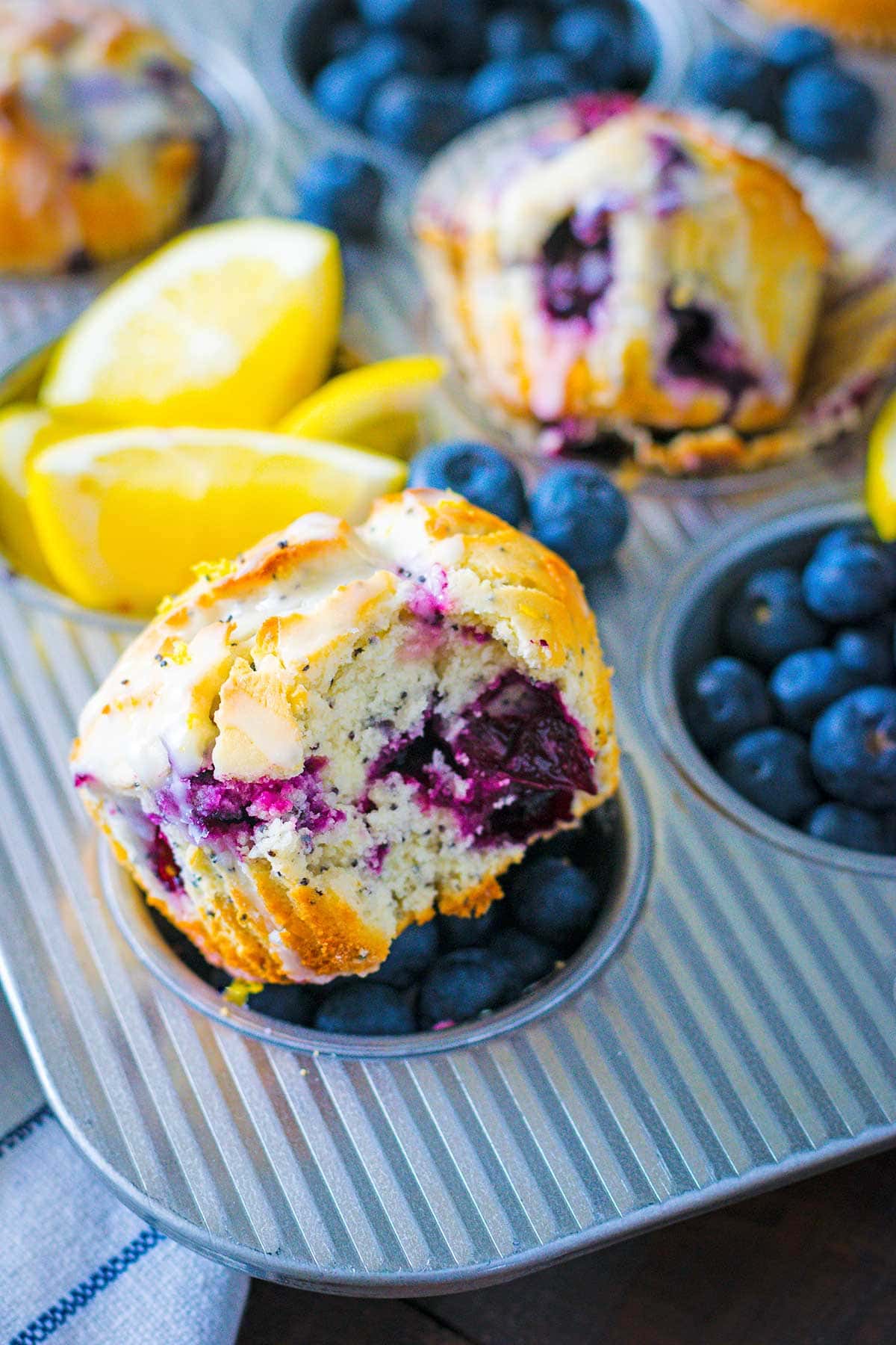 A bitten muffin on a tray with fresh lemons and blueberries.