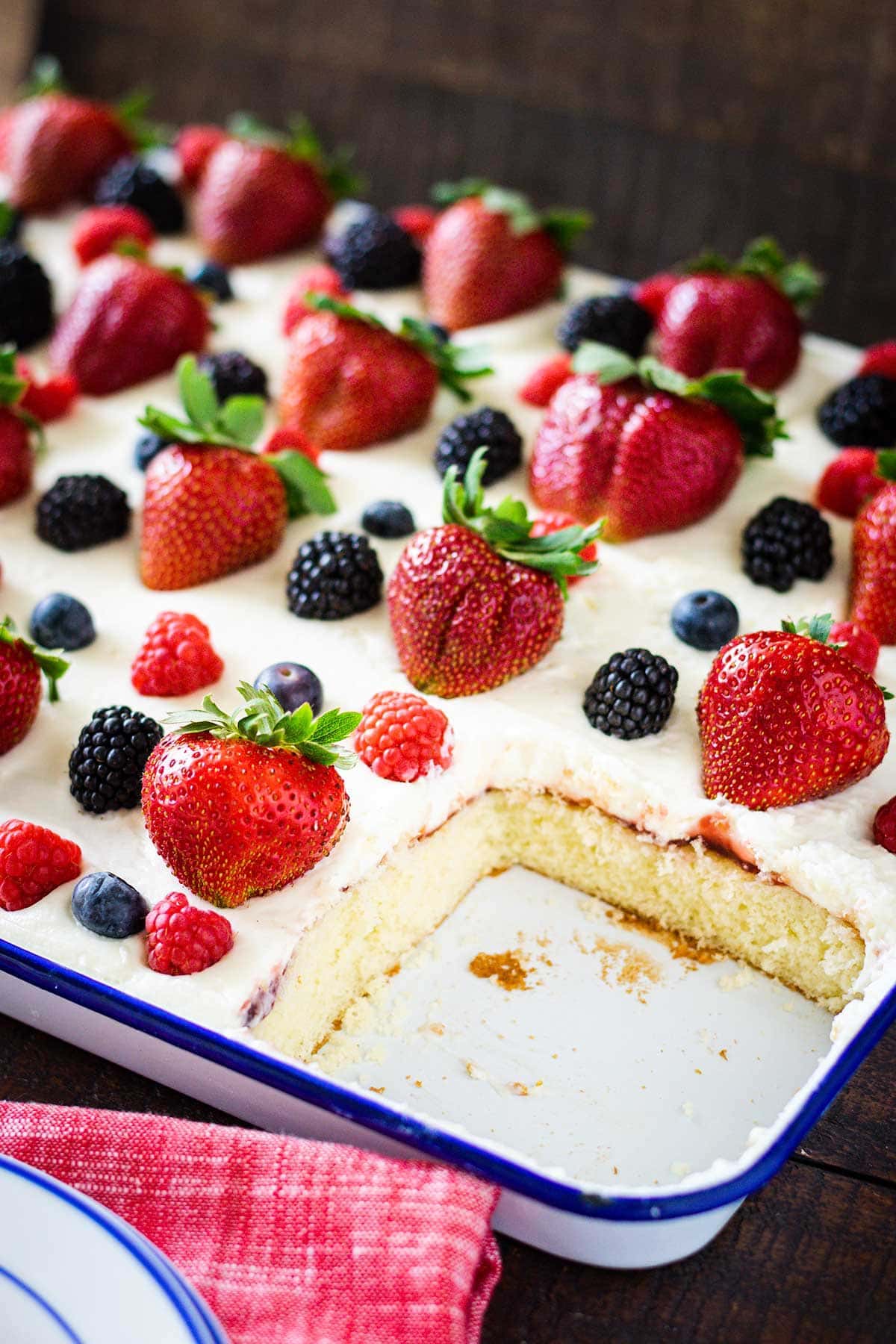 Chantilly sheet cake topped with fresh strawberries, raspberries, blueberries and blackberries. Set in a sheer pan with a slice remove showing the sponge cake.