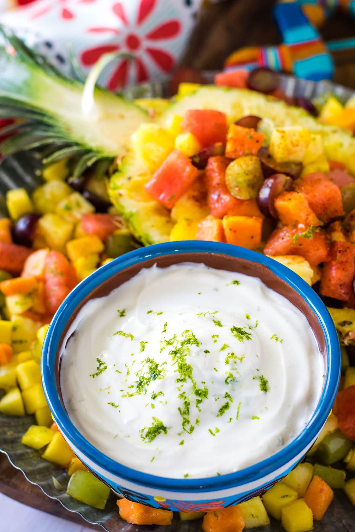 Honey lime yogurt dip on a tray with a pineapple filled with fruit. 