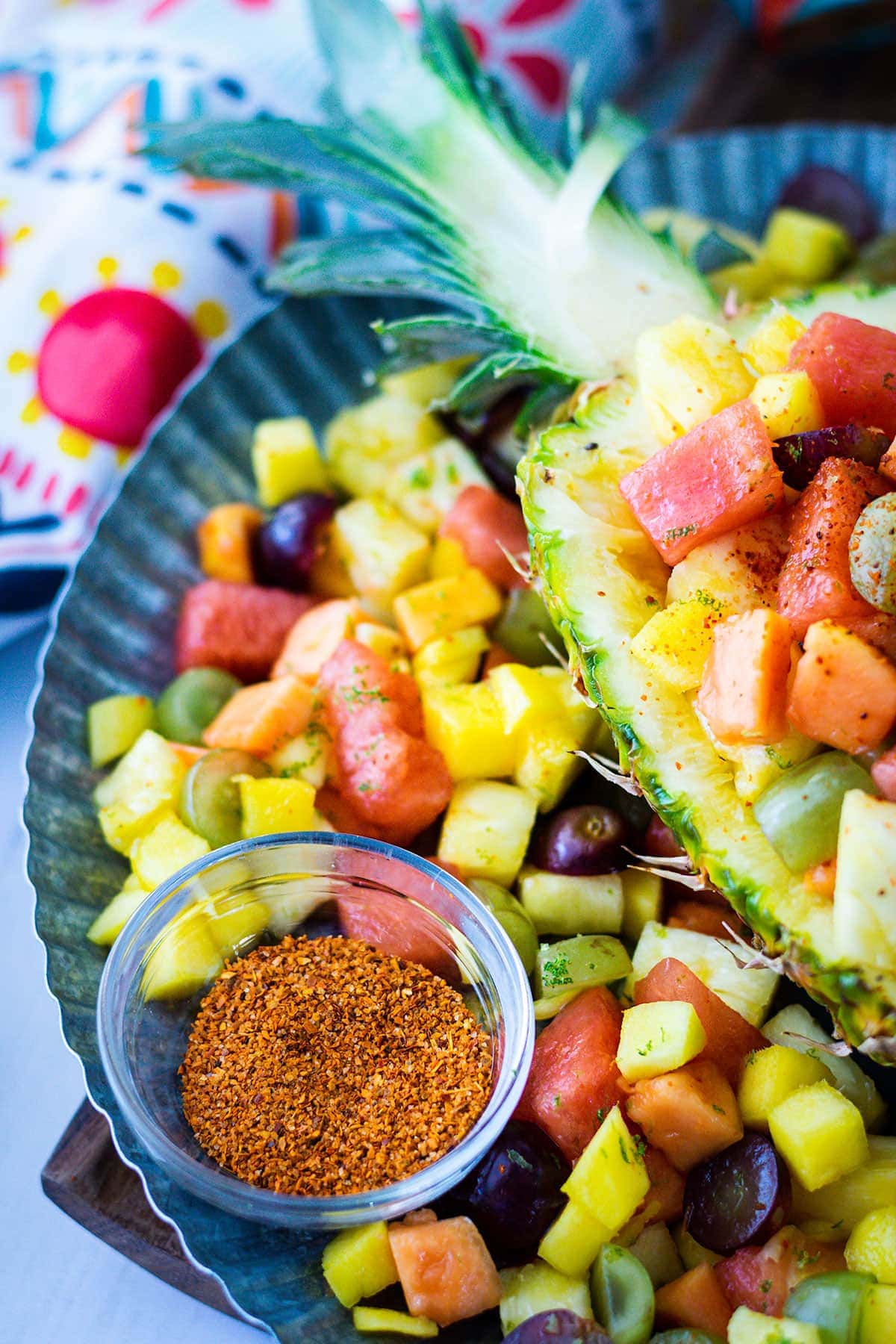 A Mexican fruit salad platter with chili lime seasoning in a clear ramekin. 