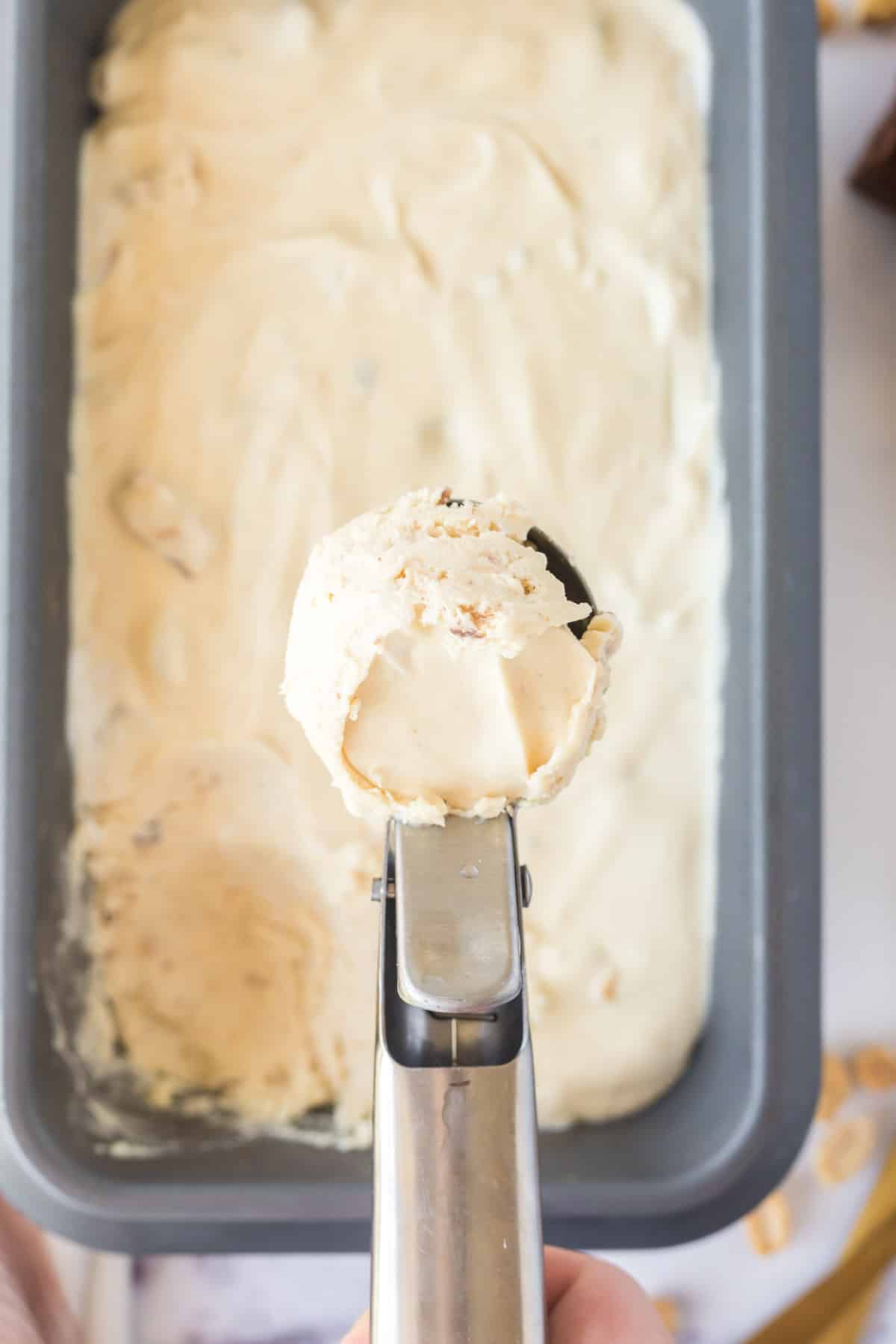 An ice cream scoop removing a scoop of nutty buddy ice cream from a loaf pan.