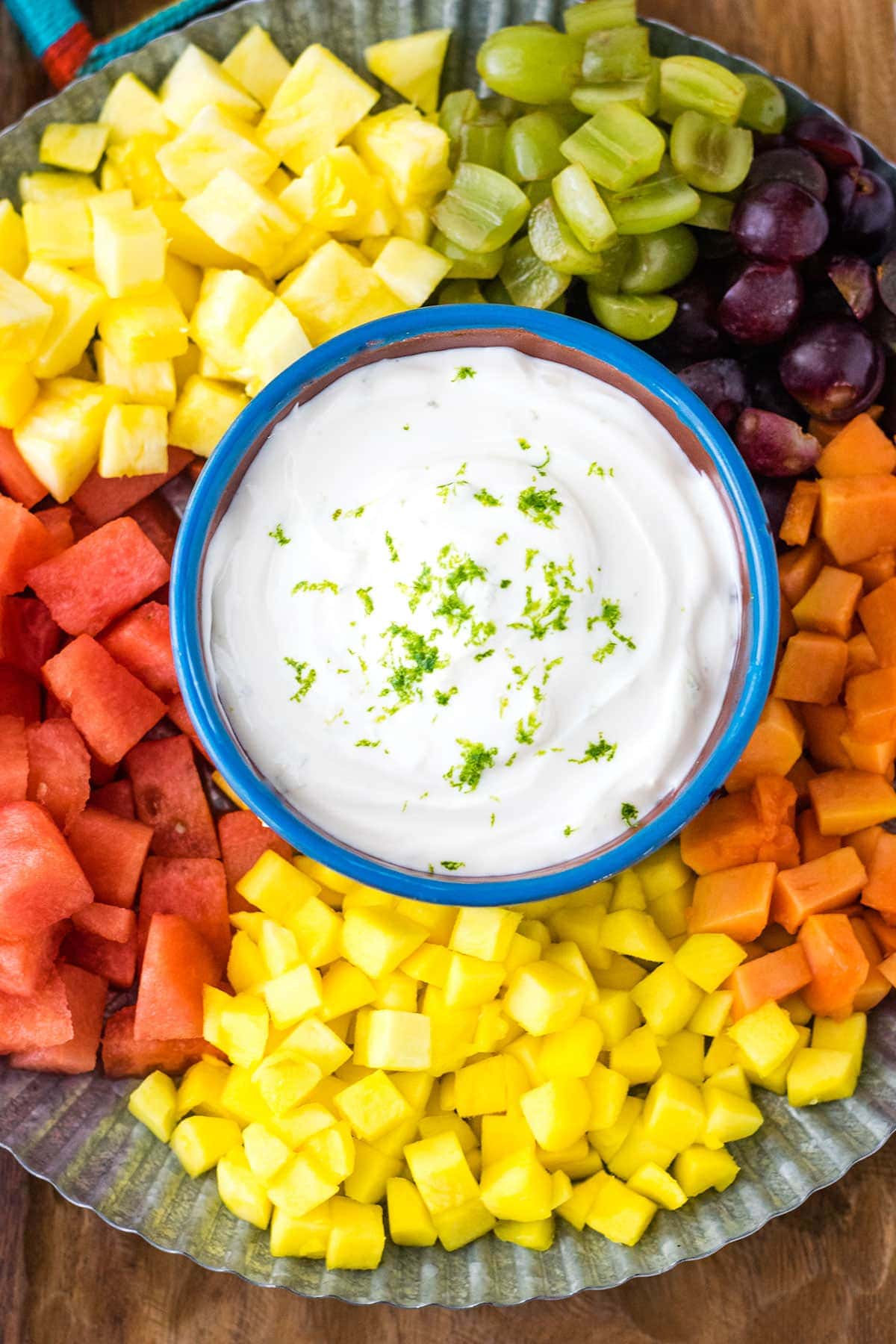 A sweet lime yogurt dip on a metal serving platter surrounded by tropical fruits.