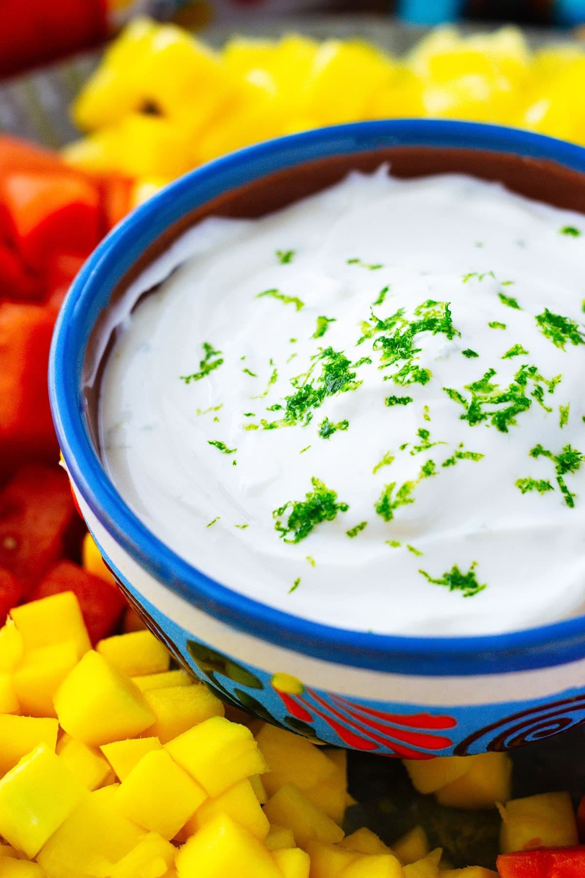 Upclose picture of honey Lime Yogurt dip garnished with lime zest in a bright blue colorful bowl .