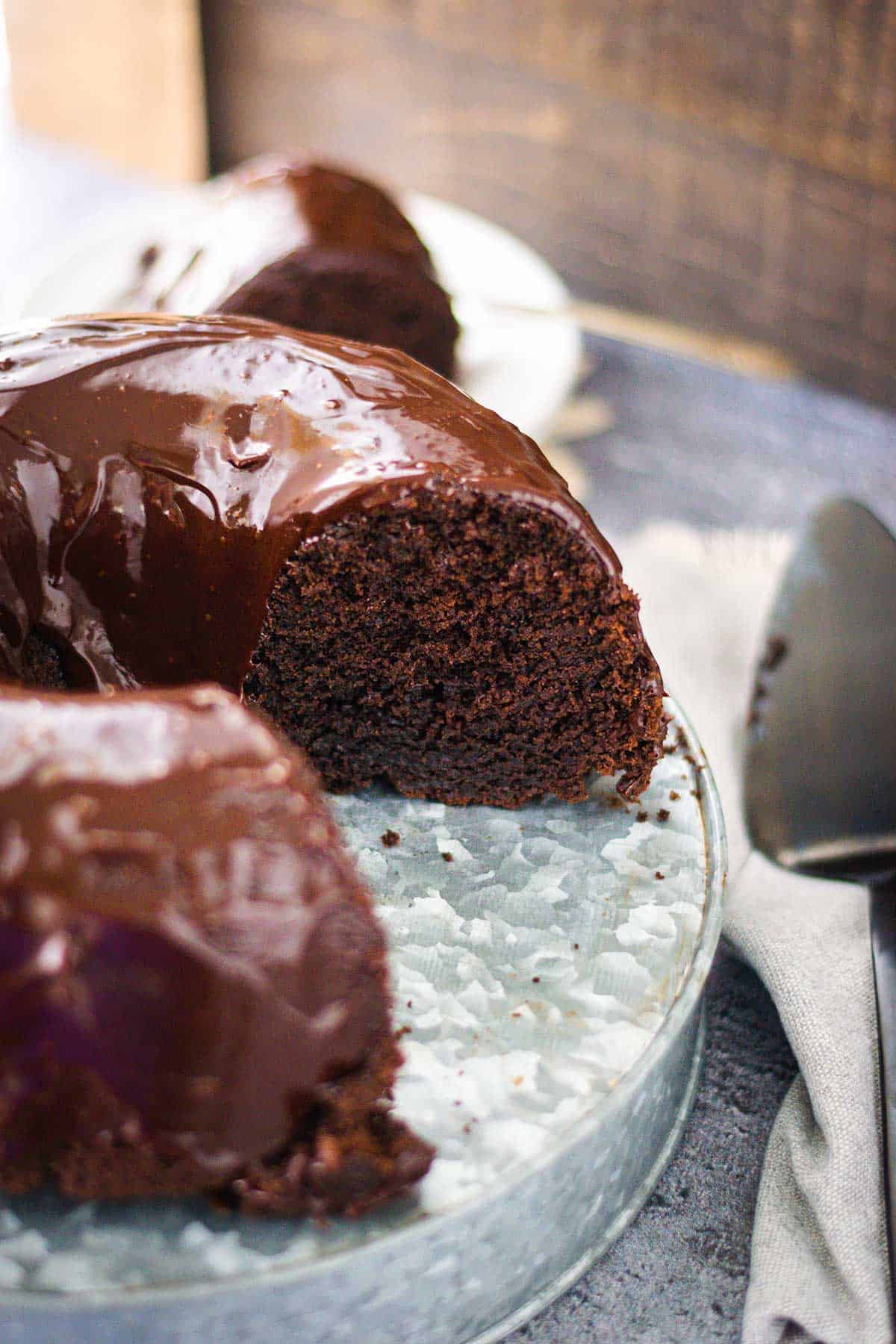 Chocolate brownie cake that has had a slice removed set on a galvanized cake server.