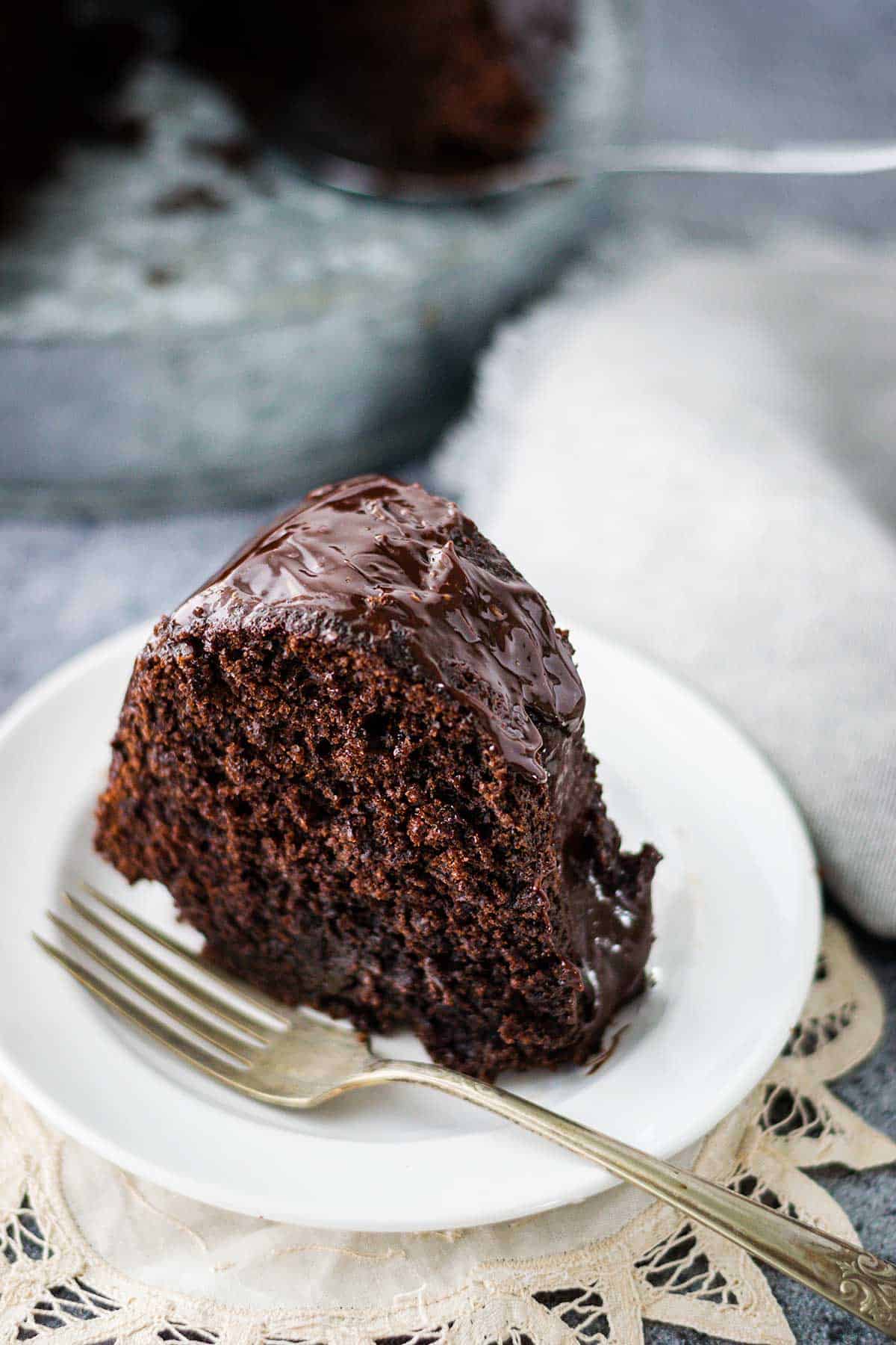 Slice of chocolate brownie cake with chocolate ganache icing on a white plate with a fork.