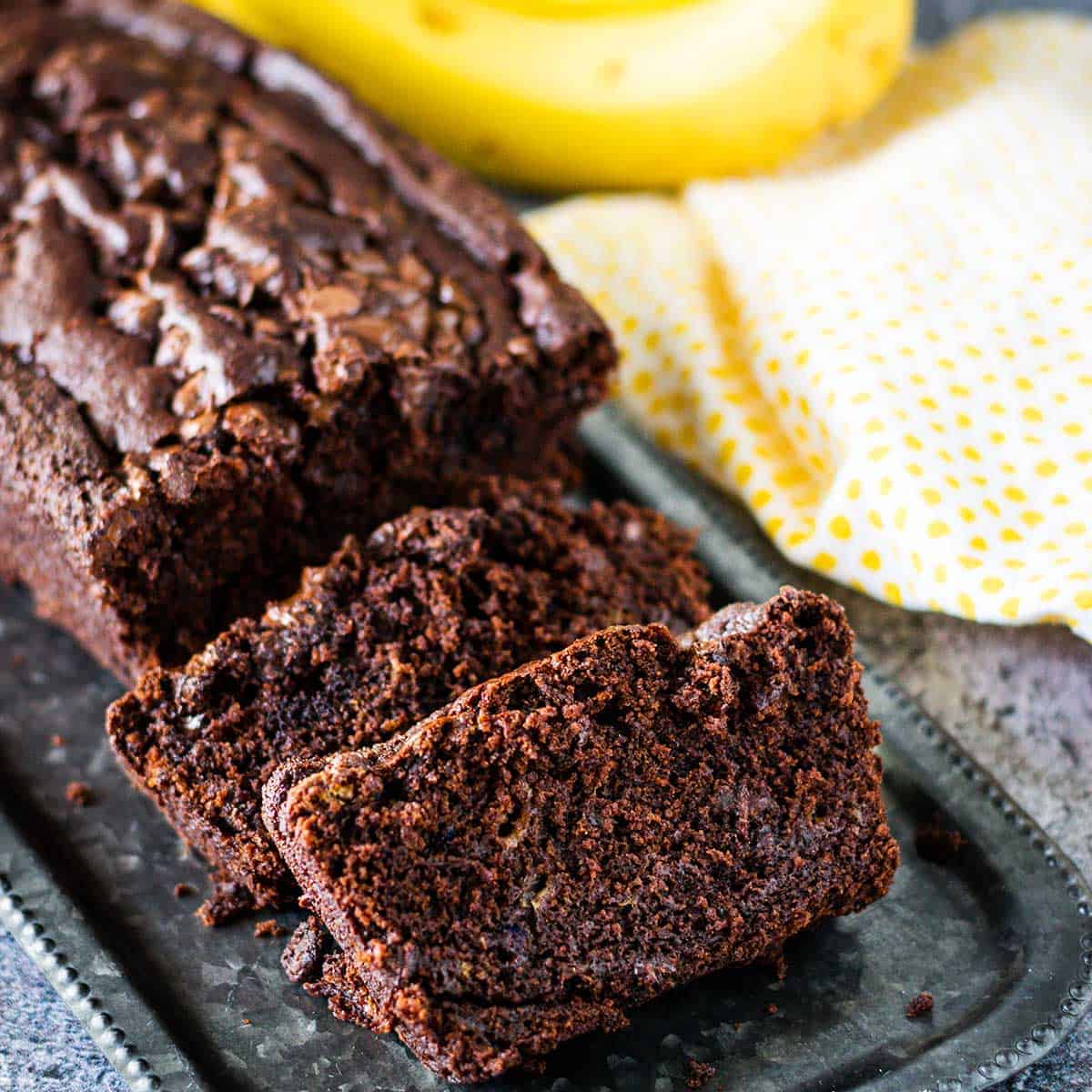 Slices of chocolate banana bread on a tray with yellow dotted napkin in background.