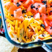 Mexican layer dip in a glass bowl with some of the dip removed.