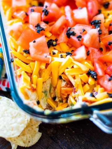 Mexican layer dip in a glass bowl with some of the dip removed.