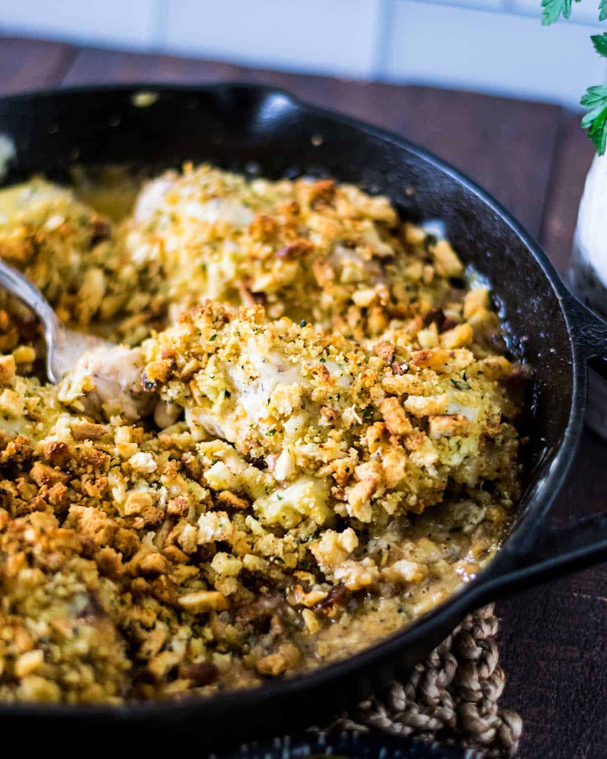 Cast-iron skillet with creamy swiss casserole being served with a serving spoon.