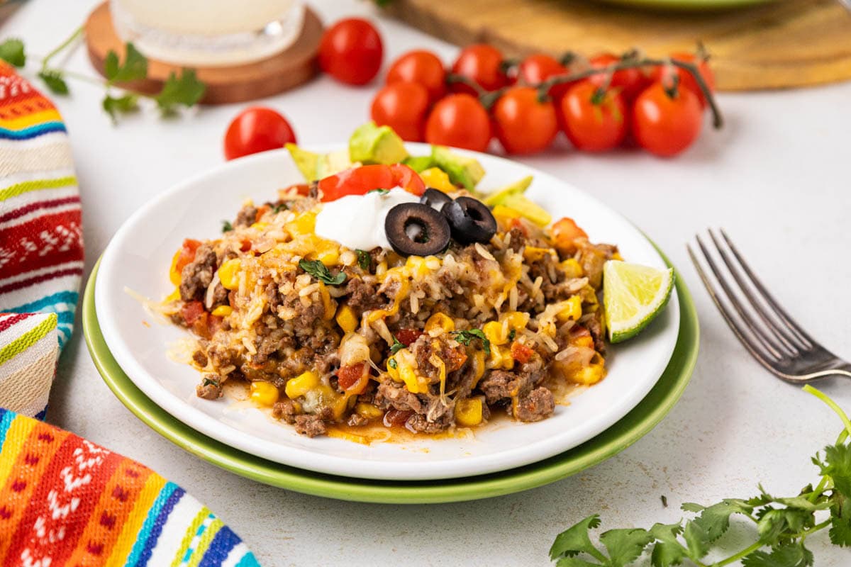A serving of tex-mex ground beef and rice on a white plate garnished with sour cream, avocado and black olives.