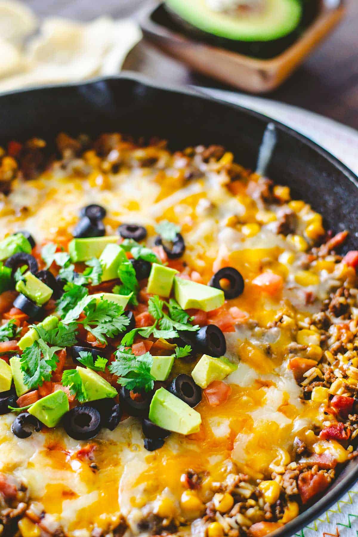 Mexican skillet rice dinner on table with sliced avocado in background.