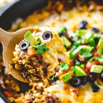 Upclose image of a scoop of ground beef and rice with cheese, avocado, black olives and tomatoes on top.