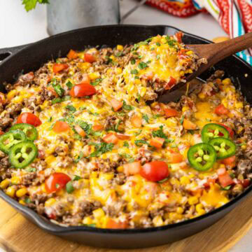 A spoon taking a serving of Mexican Beef and rice in a cast iron skillet.