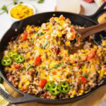 A spoon taking a serving of Mexican Beef and rice in a cast iron skillet.
