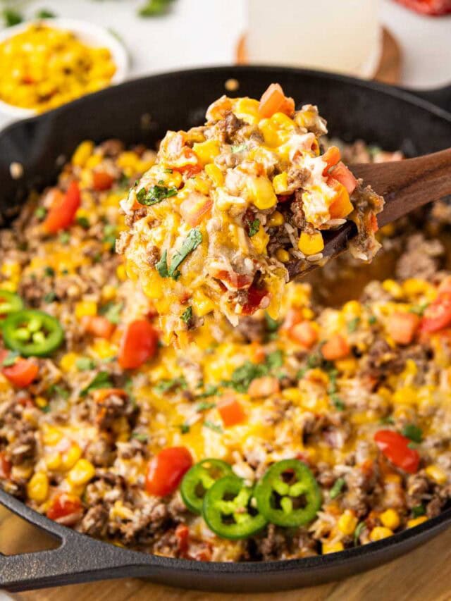 A spoon taking a serving of Mexican Beef and rice in a cast iron skillet.