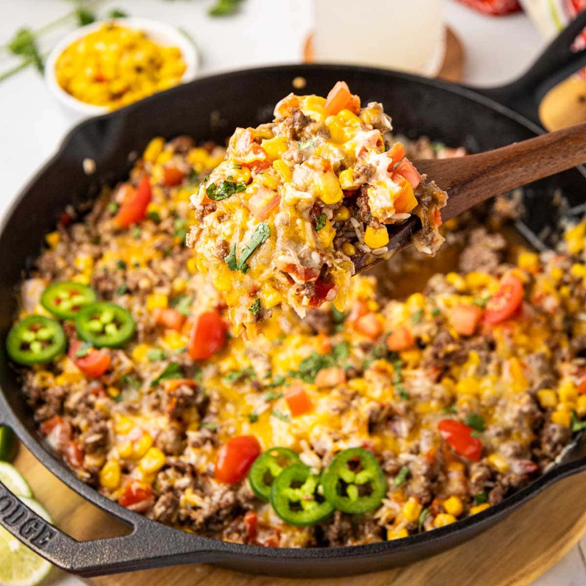 A spoon taking a serving of Mexican Beef and rice in a cast iron skillet.