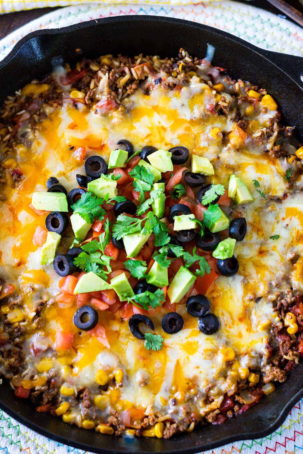 Cast iron skillet with ground beef mexican rice dish covered with melted cheese.