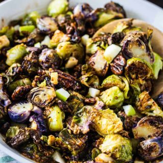 Upclose image of apple butter dijon brussels sprouts in a white serving bowl with a wooden spoon.