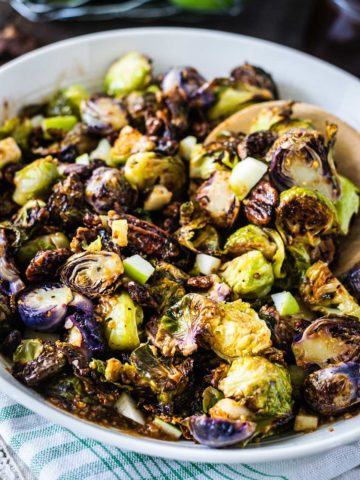 Upclose image of apple butter dijon brussels sprouts in a white serving bowl with a wooden spoon.