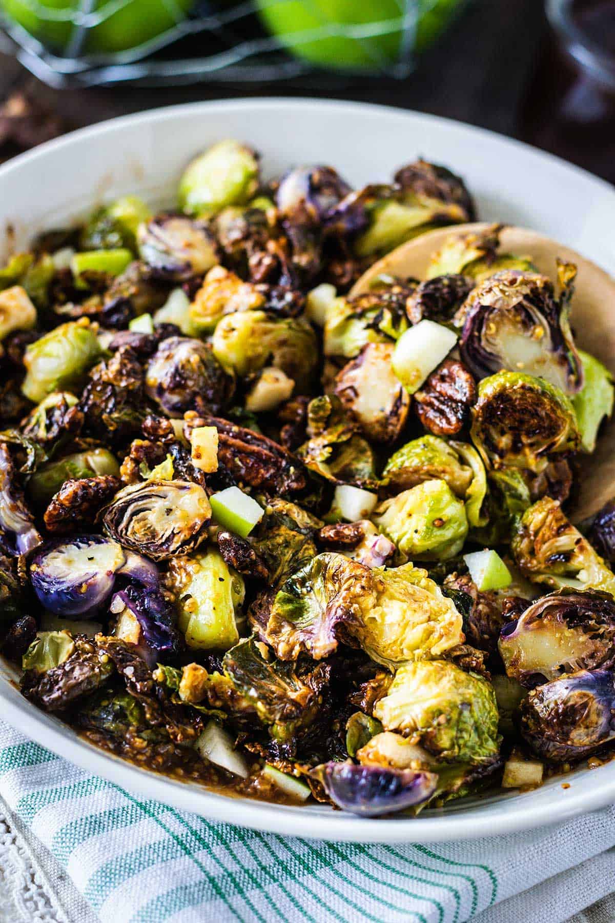 Upclose image of apple butter dijon brussels sprouts in a white serving bowl with a wooden spoon.