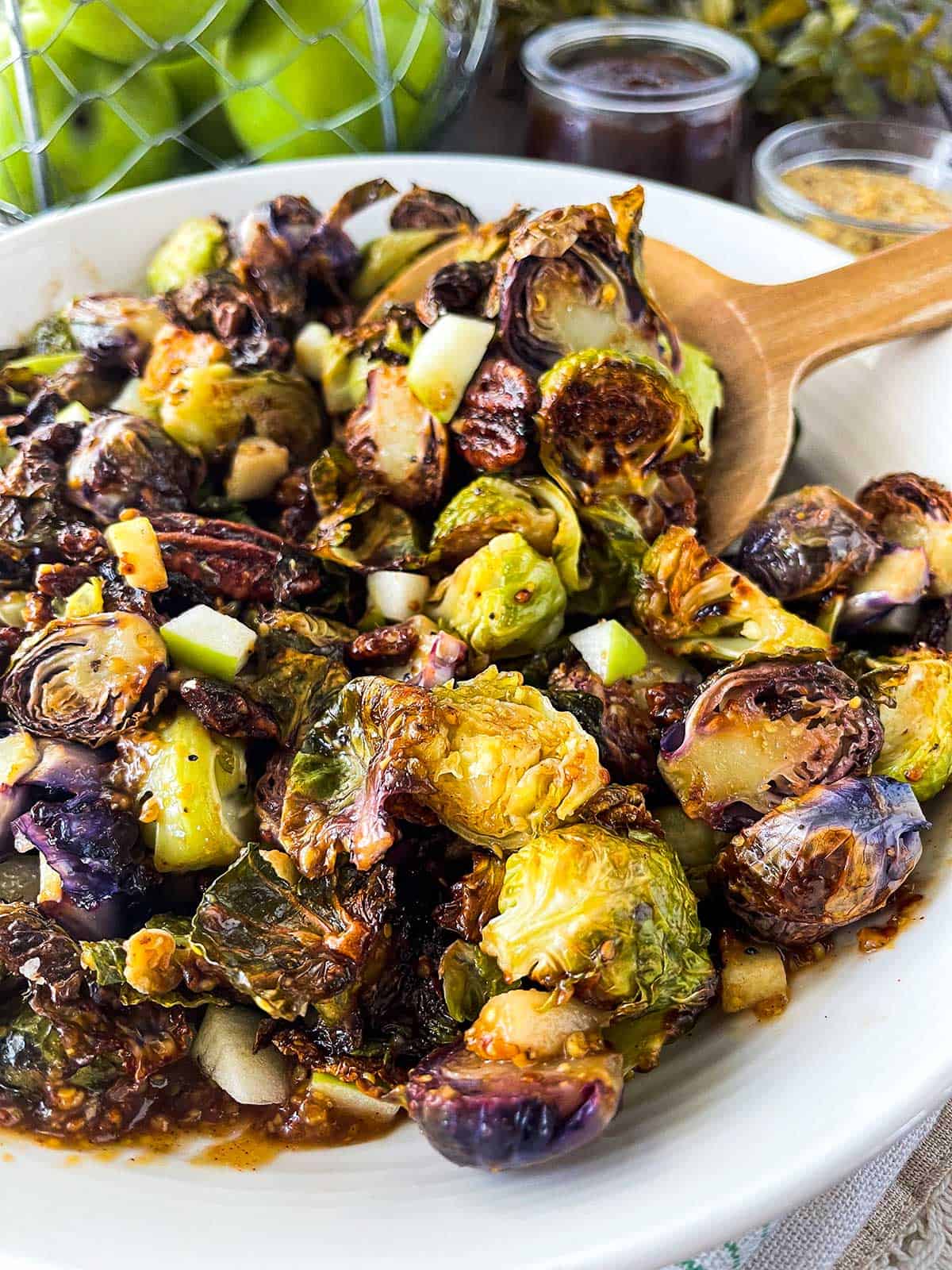 Upclose image of purple and green brussels sprouts with an apple butter dijon glaze topped with diced apples and pecans.