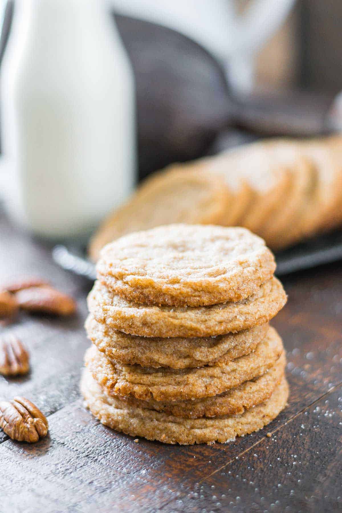 Stacked cookies on a dark wooden table with a tray of cookies in the backdrop