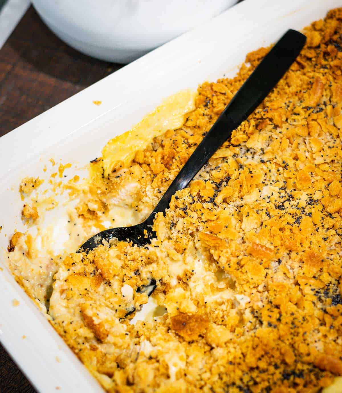 A white casserole dish with chicken poppy seed casserole scooped out of it.