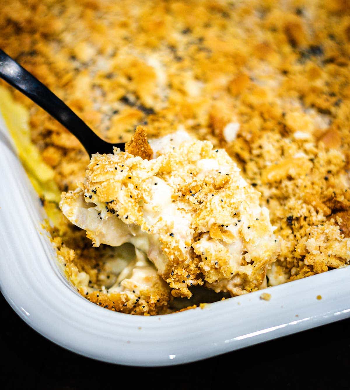 Creamy Chicken Poppy Seed Casserole being scooped and served with a black serving spoon.