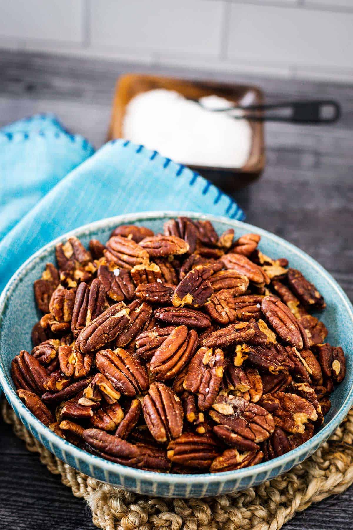 Bowl of toasted pecans sprinkled with sea salt in a blue bowl set on a wooden table.