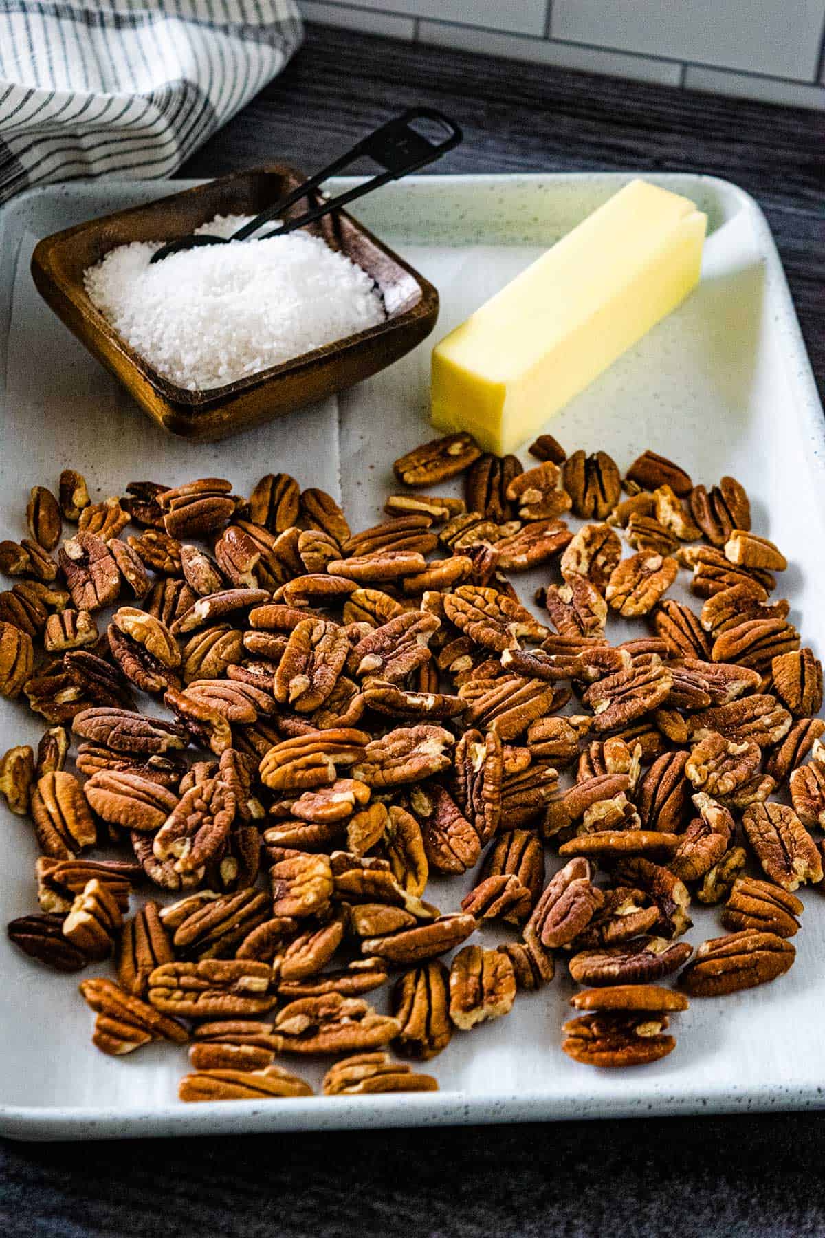 Toasted pecan ingredients pecans, butter, and salt on a white baking tray.