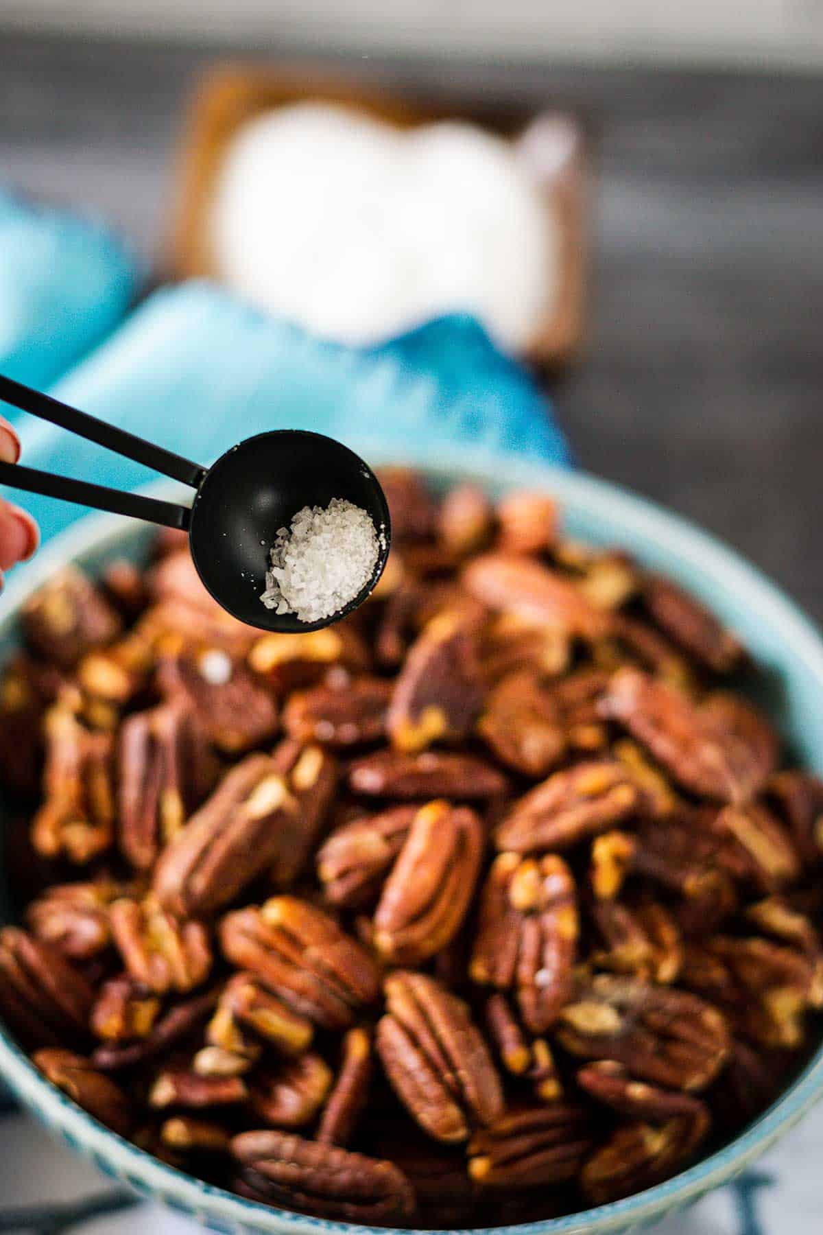 Toasted pecans in a blue bowl being topped with salt.