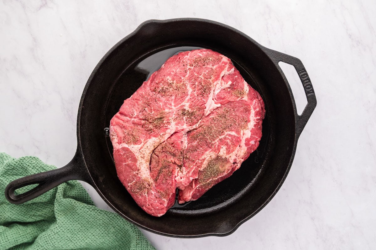 A hot cast iron skillet with the seasoned chuck roast in it.
