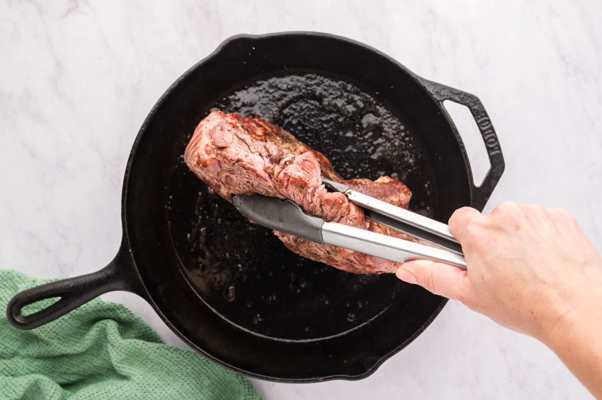 Flipping a seared chuck roast with tongs.