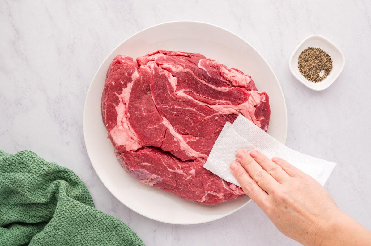 Patting a chuck roast with a paper towel to dry it.