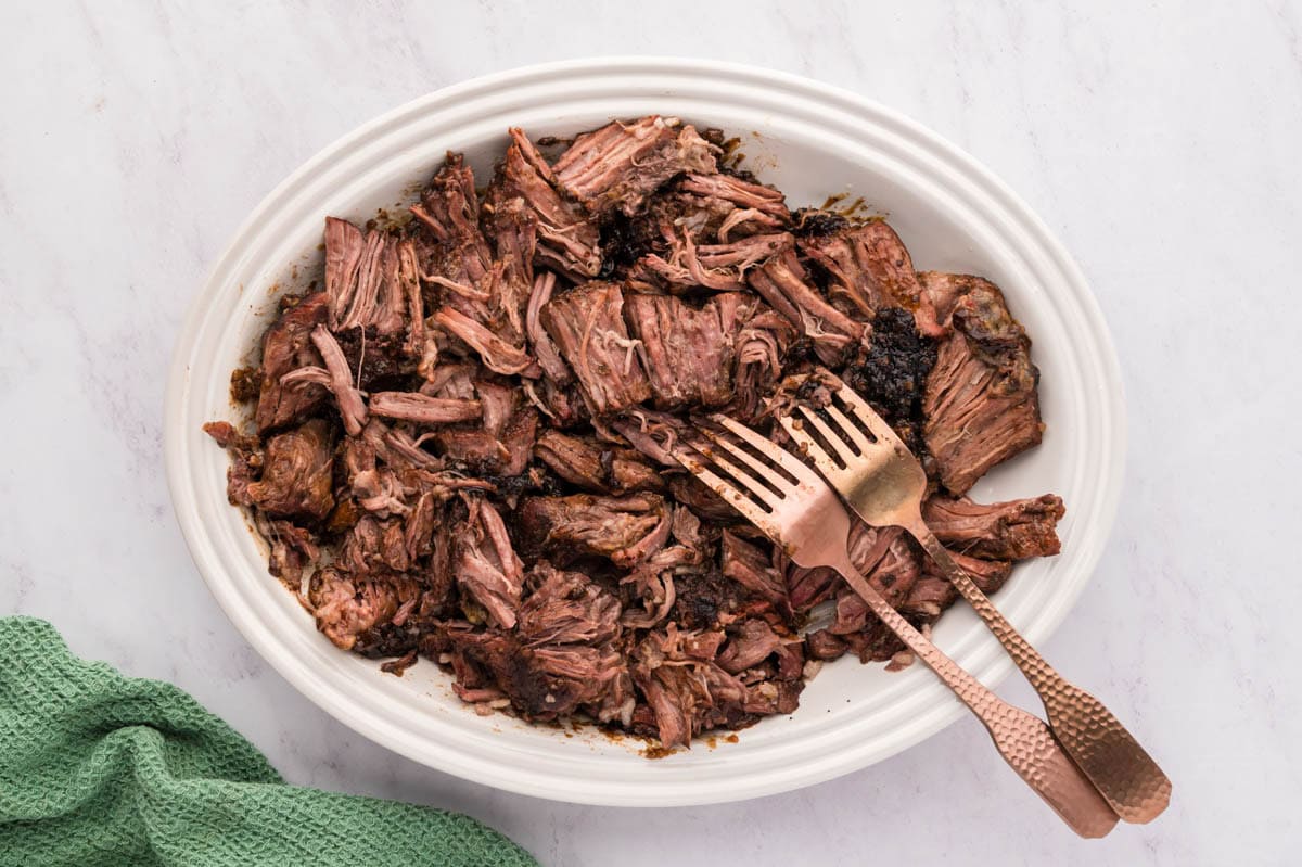 Shredded pot roast on a platter with 2 forks.