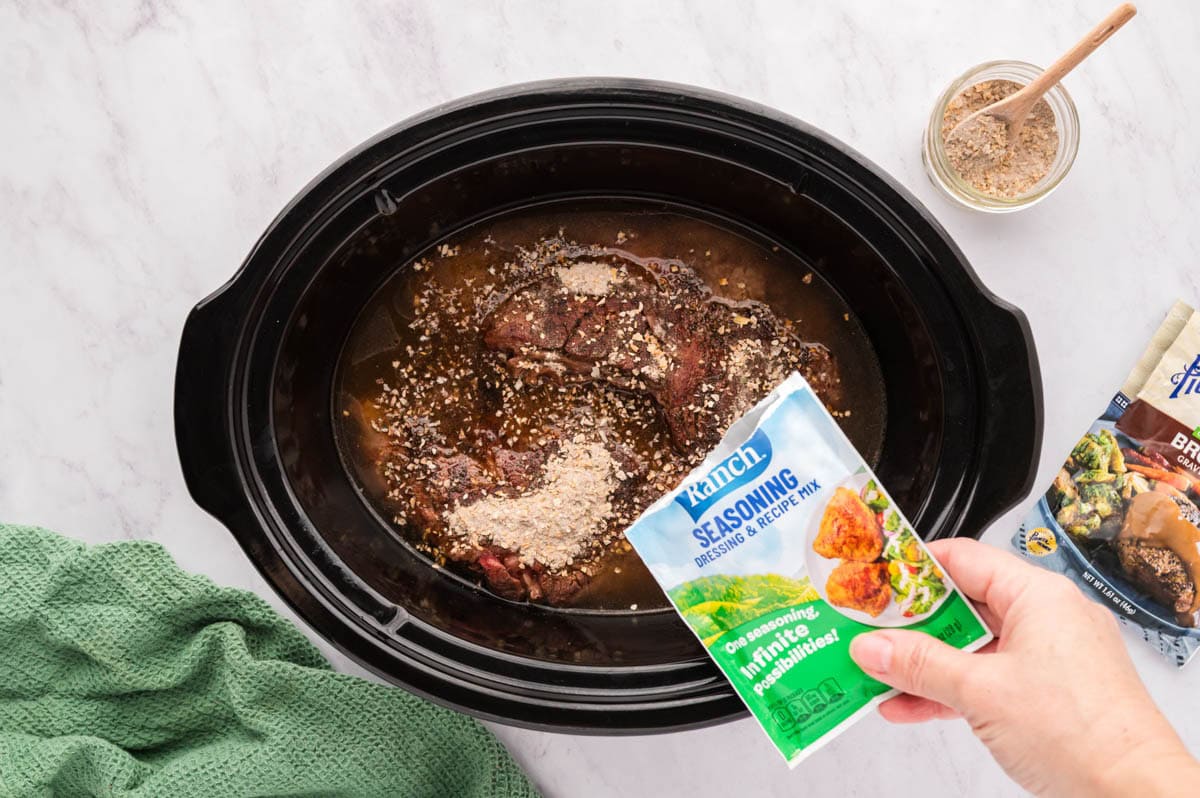 Sprinkling the ranch packet on top of the chuck roast.