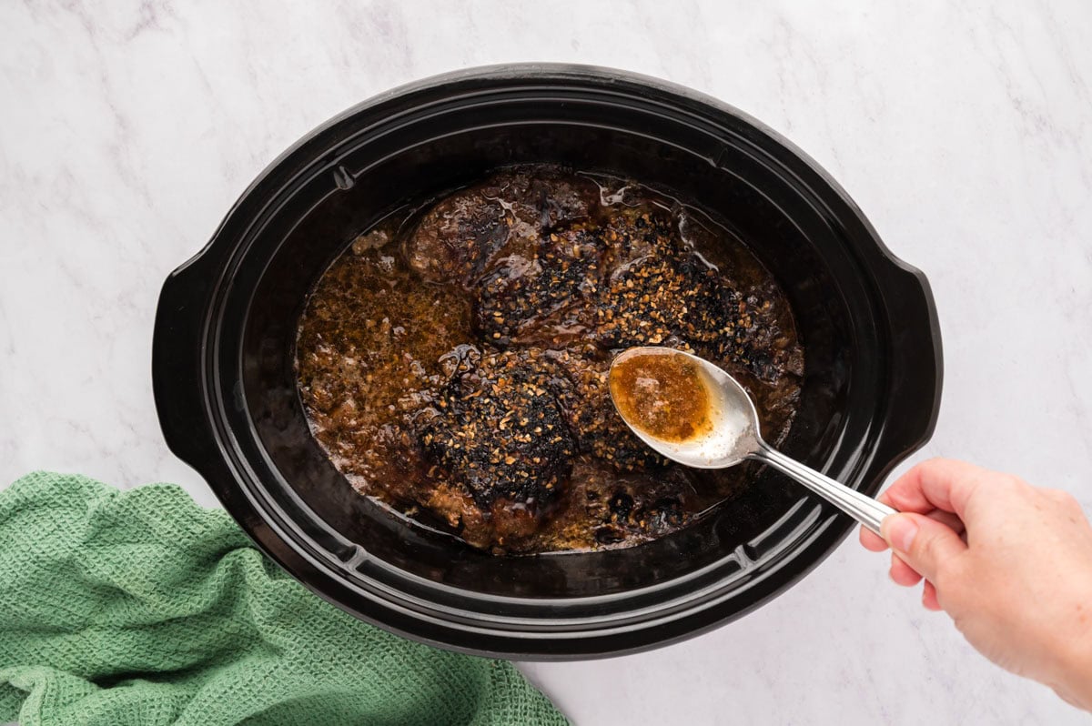 Spooning juices over the top of the roast in the slow cooker.