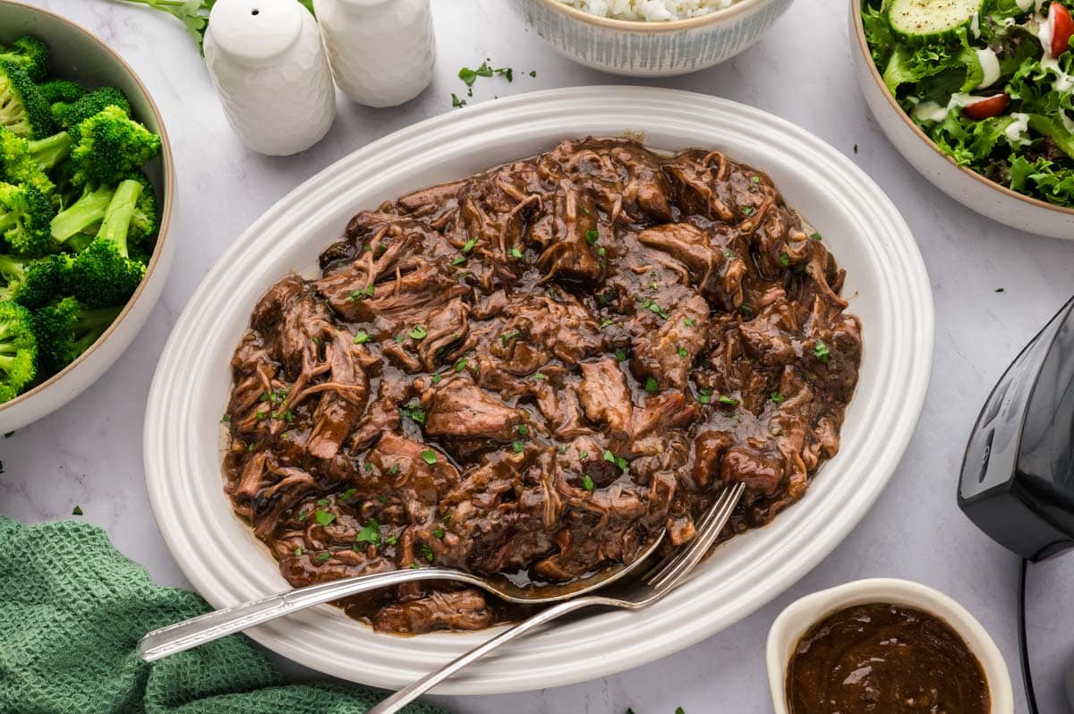 Shredded 3 packet pot roast with gravy on an white oval serving platter.