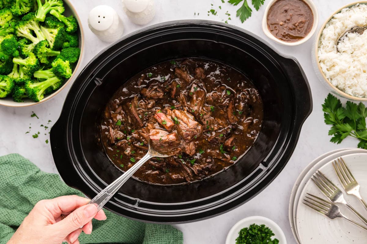 A spoon removing a serving of 3 envelope roast from the slow cooker.