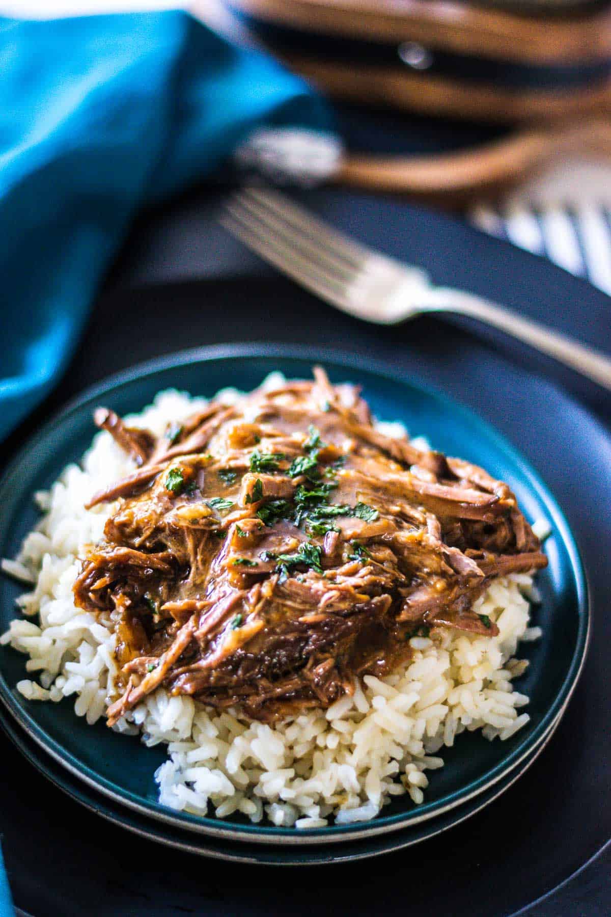 Shredded 3-packet pot roast with gravy over rice on a black plate.