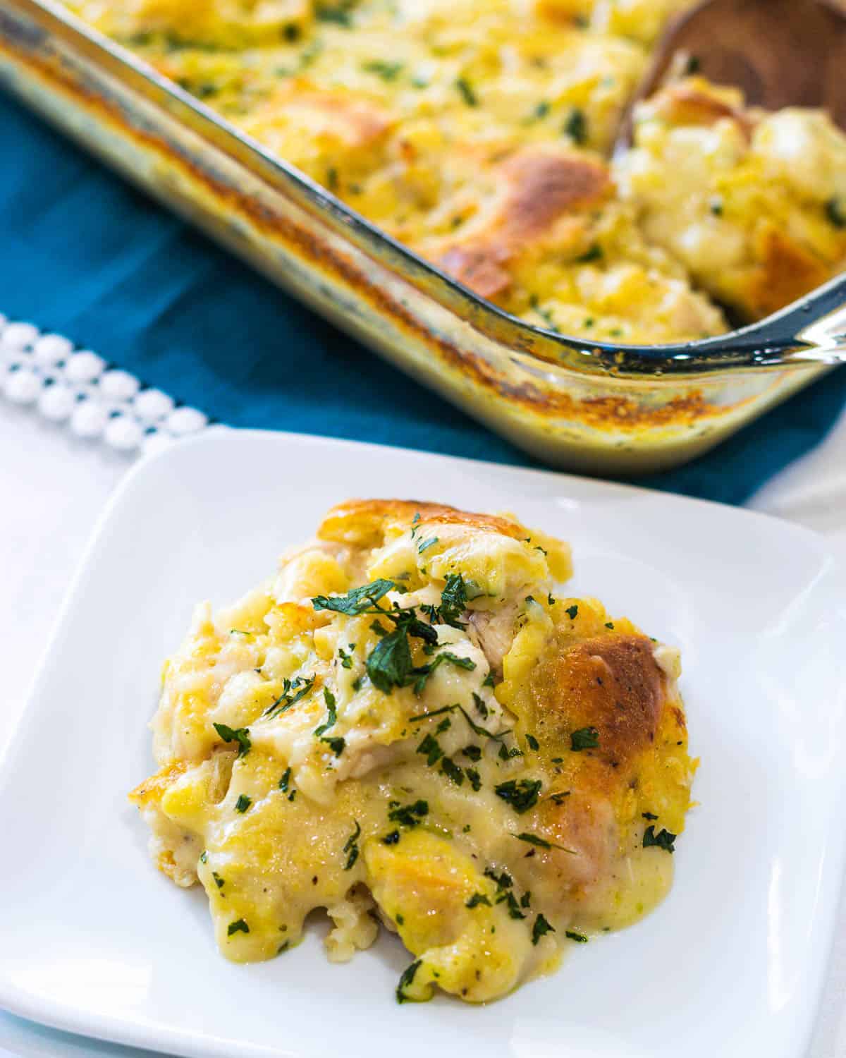 A white plate filled with chicken and dumpling casserole with the casserole dish in the background.