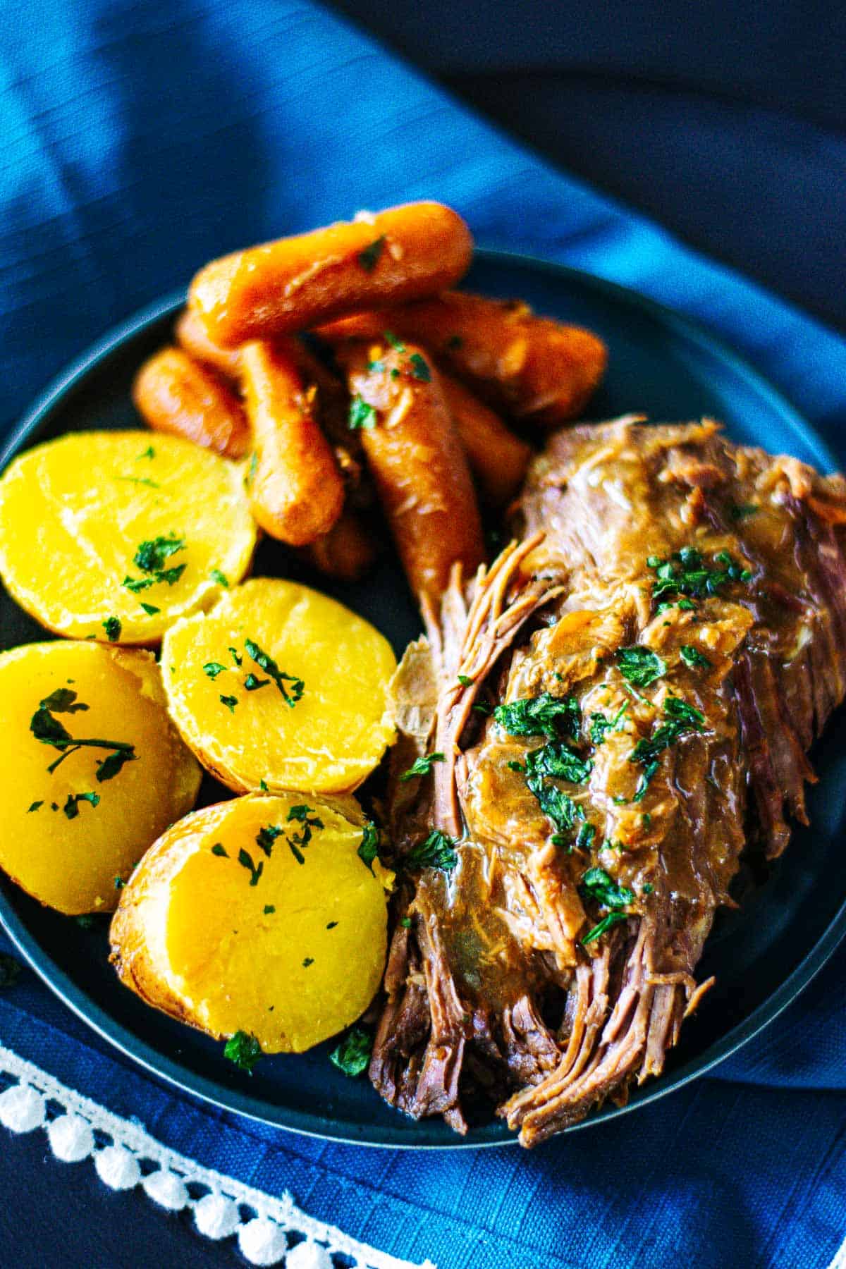 Tender Pork Roast topped with gravy and parsley plated with potatoes and carrots.