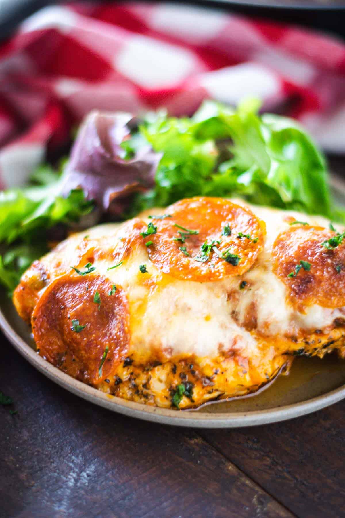 Gooey Cheesy Pizza Stuffed Chicken on a grey plate with a green salad.