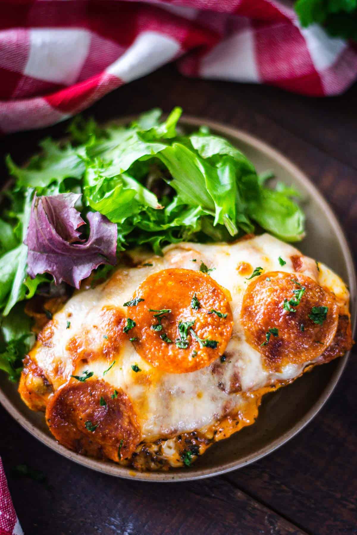 Overhead image of baked pizza chicken plated with a green salad.