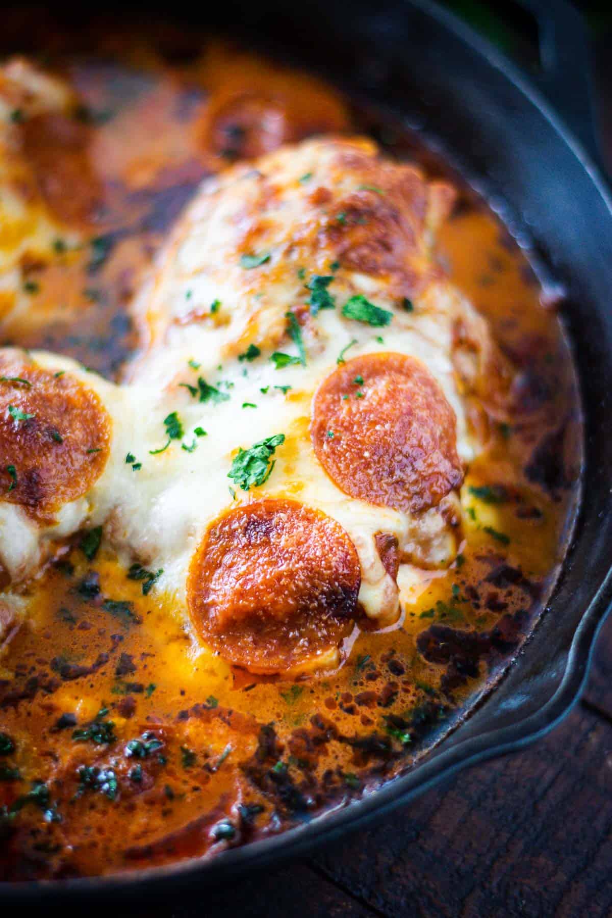 Stuffed Pizza Chicken baked in a cast iron skillet garnished with parsley.