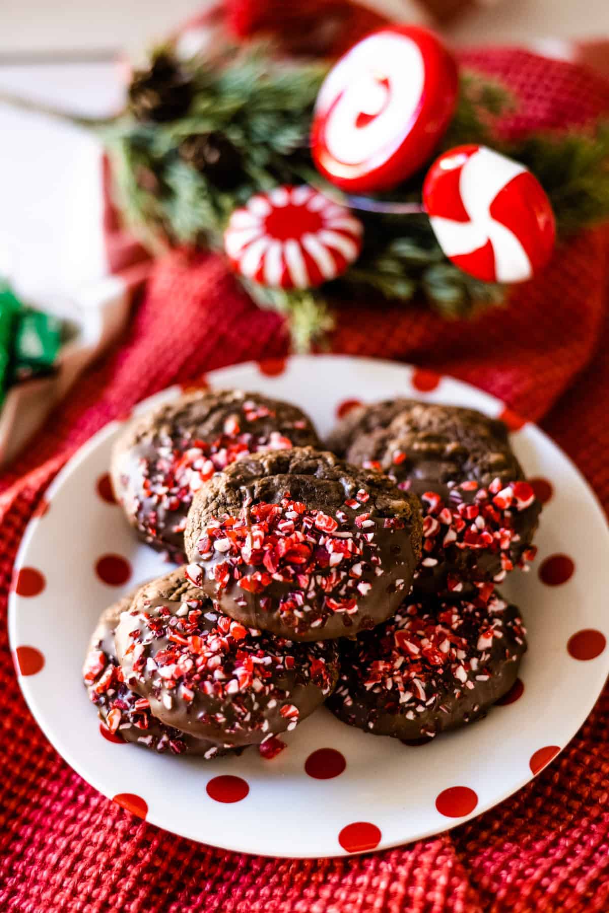 Peppermint brownie mix cookies on a white plate with red polka dots on a red placemat with peppermint decor in the background.